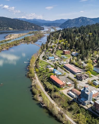 Aerial view of riverside town nestled between forested mountains and multiple lakes with winding roads and scattered buildings