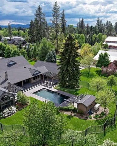 Aerial view of modern home with pool surrounded by tall evergreen trees and manicured lawn, rural valley setting