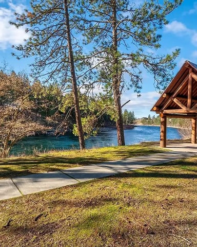 Wooden pavilion on grassy lakeside clearing surrounded by pine trees and blue water