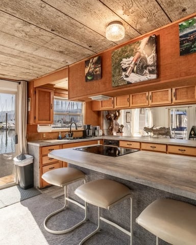 Houseboat kitchen with wood cabinets, island seating, and marina view through glass doors