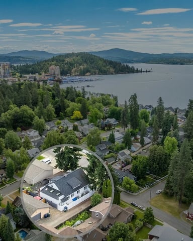 Aerial view of lakeside residential neighborhood with modern home highlighted, forested mountains and downtown skyline across the water