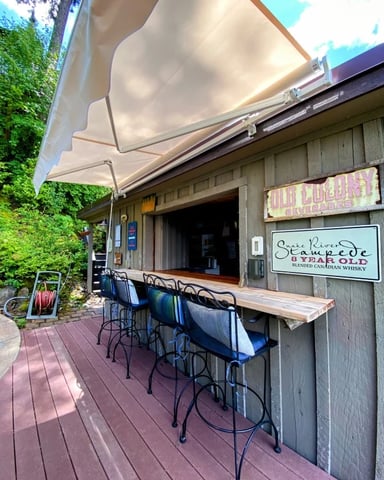 Outdoor patio bar with retractable awning, wooden counter, metal bar stools, and ivy-covered walls