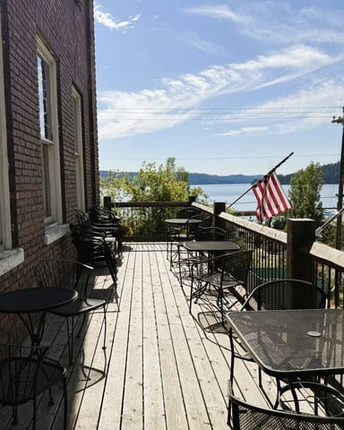 Waterfront deck with dining tables, brick building, lake view, and American flags