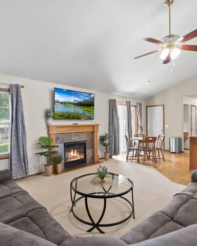 Open-plan living room with gray sectional sofa, fireplace, ceiling fan, and view to kitchen and dining area